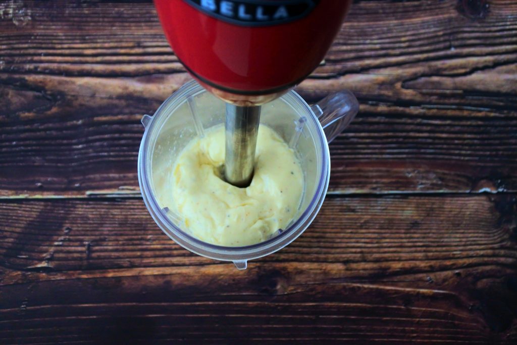 An overhead image of mayonnaise being blended in a jug with a stick blender in it