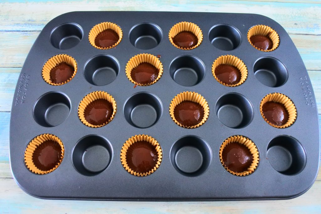 An angled overhead image of a mini muffin tin with paper liners filled with chocolate