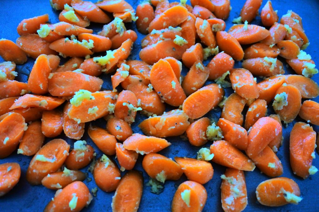 A head on close up image of uncooked honey-glazed carrots on a baking tray