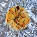 Overhead image of a cut and roasted head of garlic on foil paper