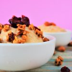 a close up image of a bowl of banana ice cream topped with and surrounded by homemade granola and dried cranberries.