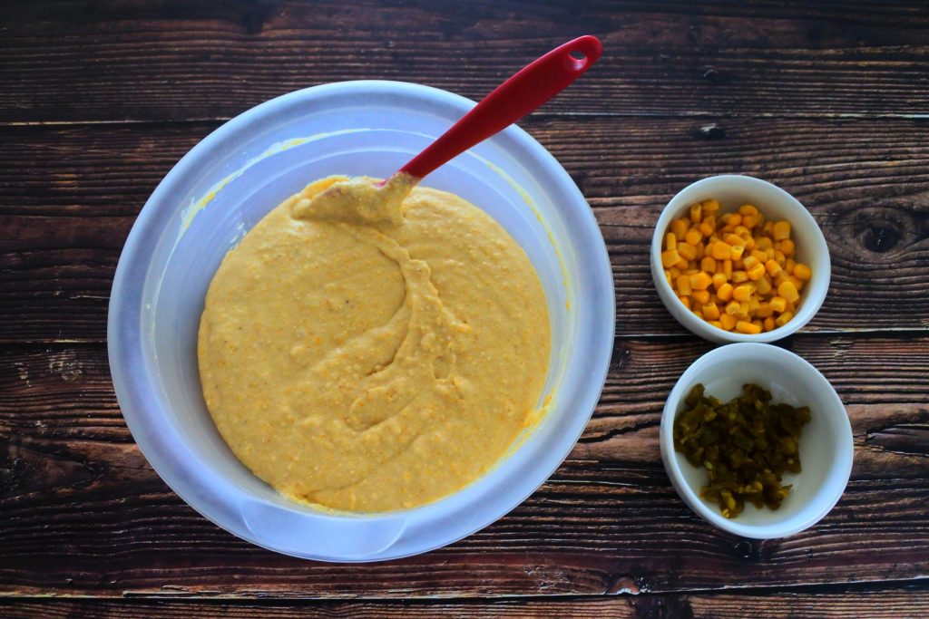An overhead image of a bowl of cornbread batter with diced jalapeno and sweet corn kernels on the side in small bowls