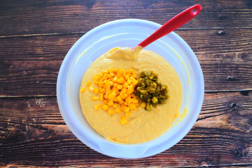 An overhead image of a bowl of cornbread batter with diced jalapeno and sweet corn kernels added in