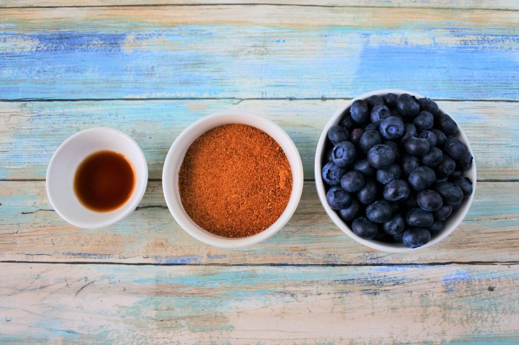 An overhead image of dishes containing vanilla extract, coconut sugar and fresh blueberries