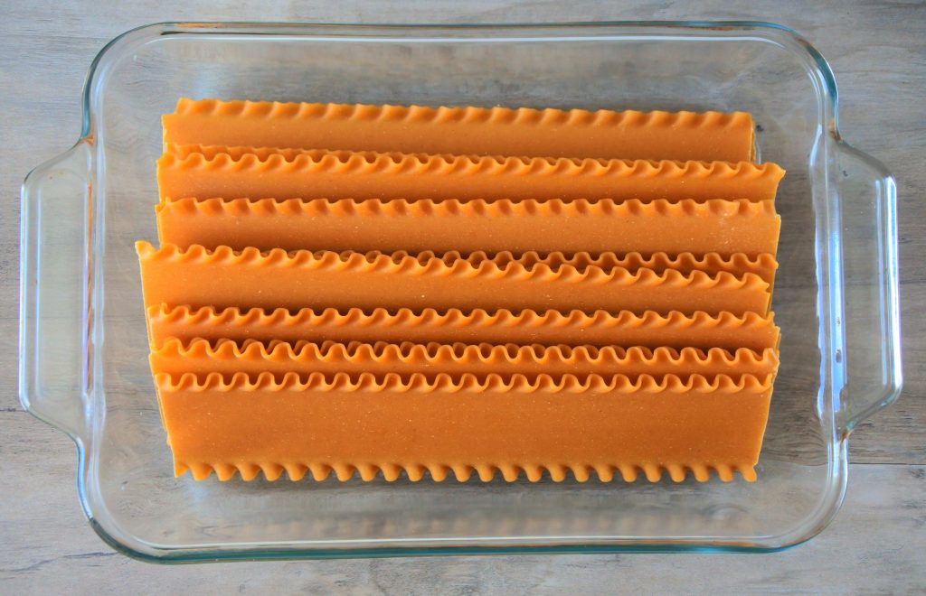 An overhead image of a glass dish with uncooked sheets of whole wheat lasagna pasta