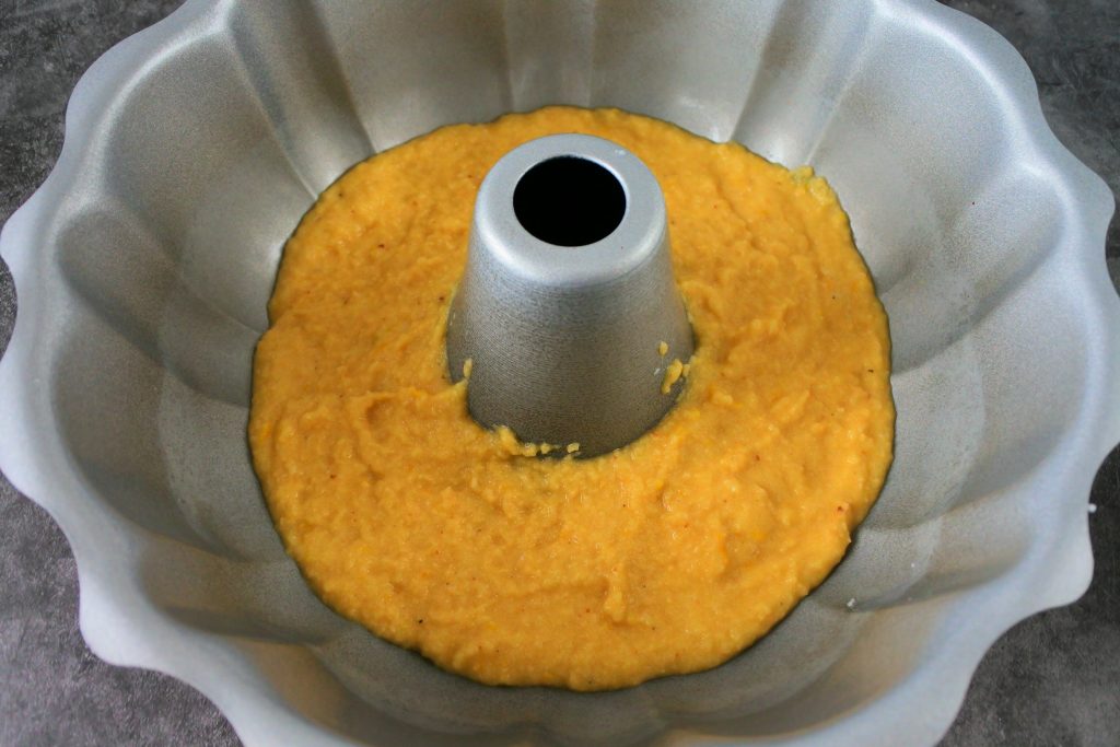 An overhead image of some batter being added to the bottom of a greased bundt pan