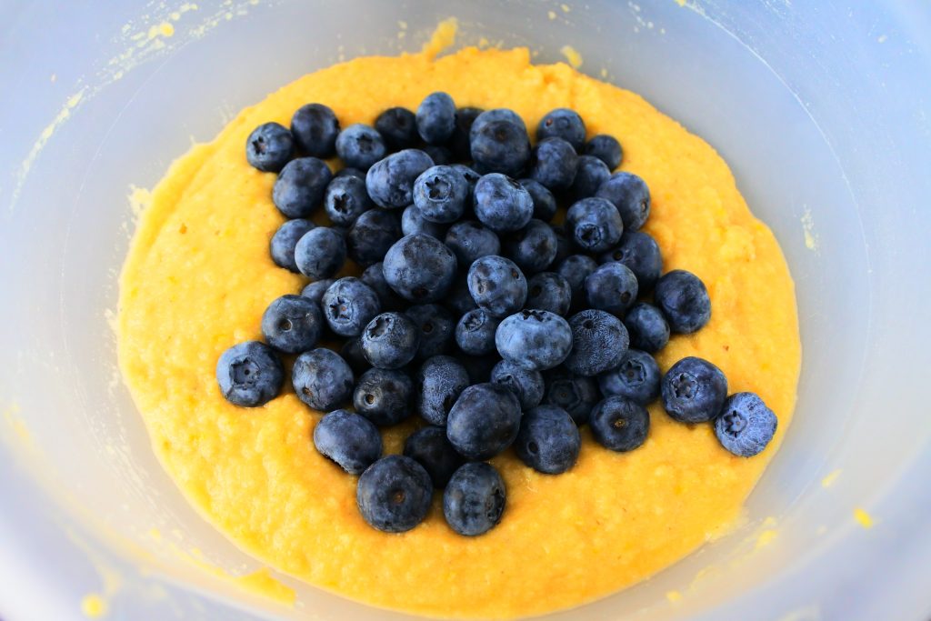 An overhead image of fresh blueberries being added to the mixed cake batter
