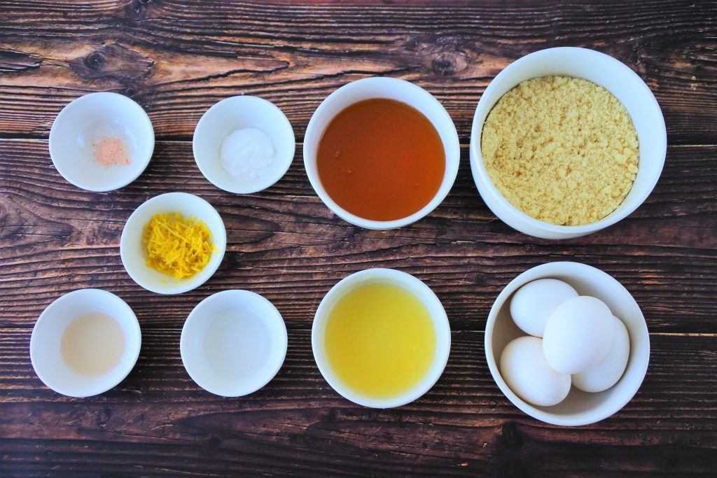Overhead image of bowls containing the following ingredients: almond flour, eggs, honey, lemon juice, lemon zest, lemon extract, vanilla extract, salt, baking soda and baking powder