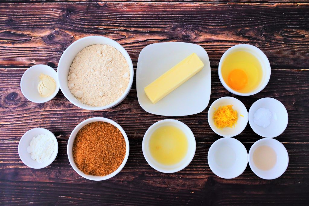 An overhead image of bowls of ingredients for lemon cookies including vital wheat gluten, whole wheat flour, potato starch, raw organic cane sugar, butter, lemon juice, an egg, lemon zest, baking powder, lemon extract and vanilla extract.