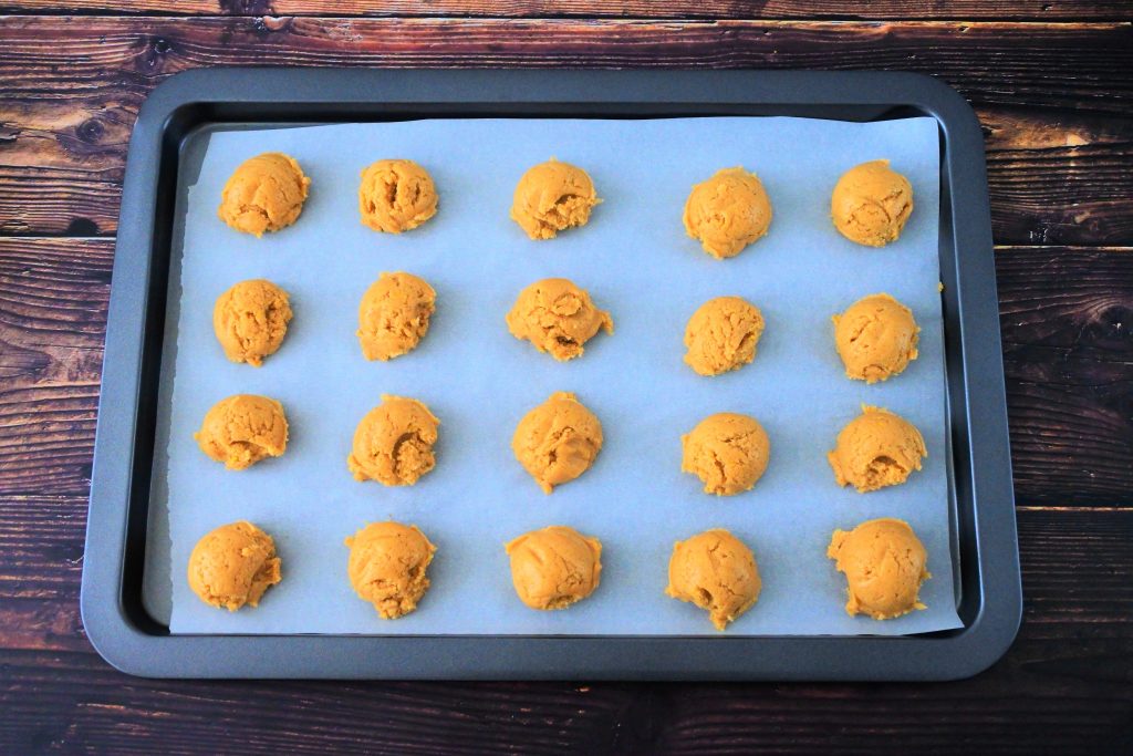 An angled image of a parchment lined baking tray with twenty balls of lemon sugar cookie dough