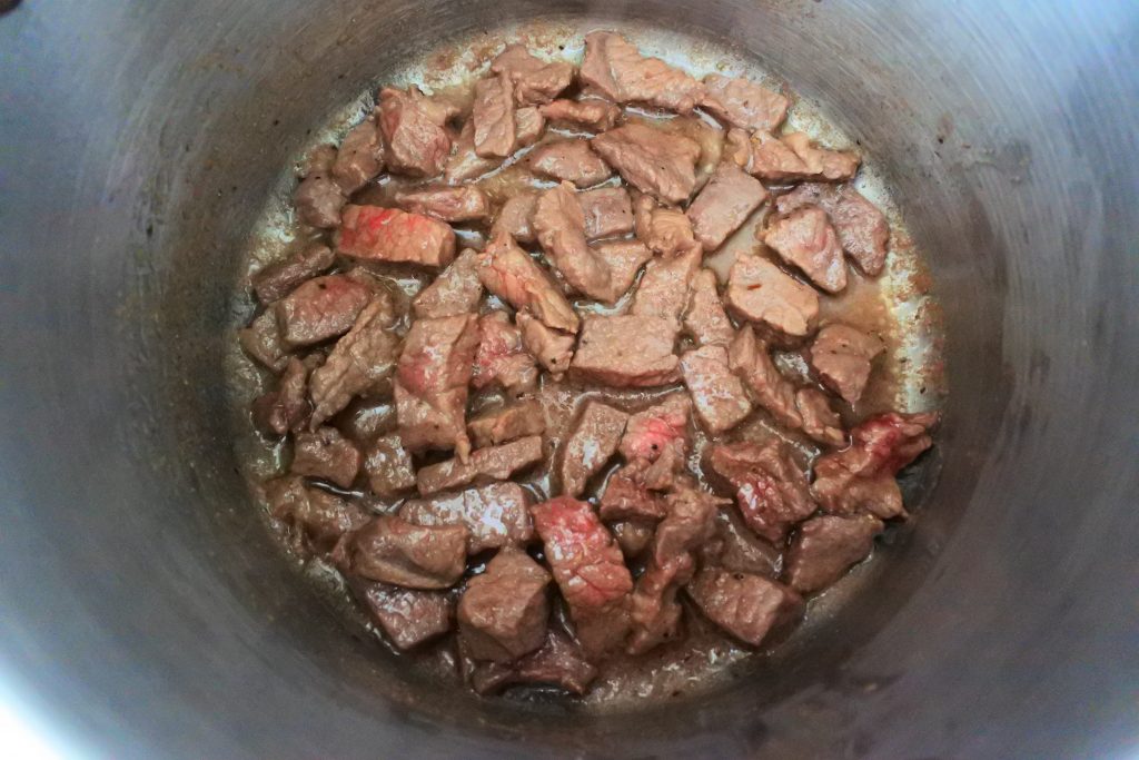 An overhead image of a pot with pieces of seasoned beef being cooked