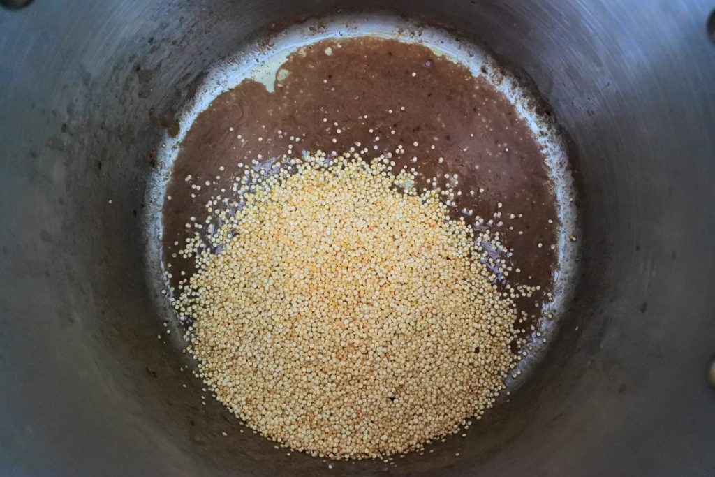 An overhead image of a pot with uncooked quinoa added to liquid leftover from cooked beef