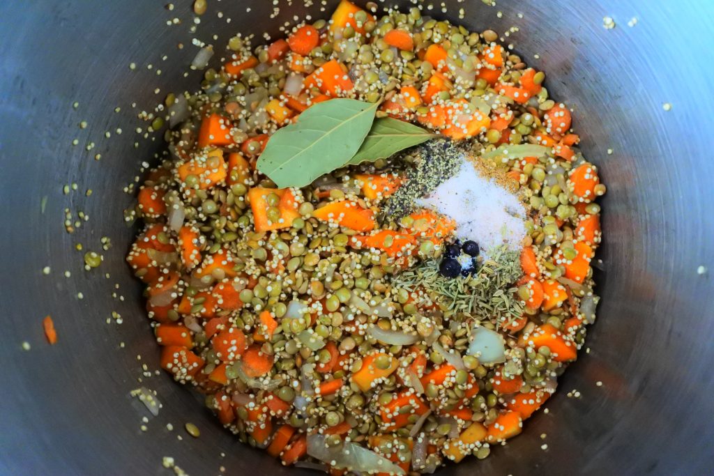 An overhead image of a pot of onions, carrots, butternut squash, quinoa, lentils, and spices