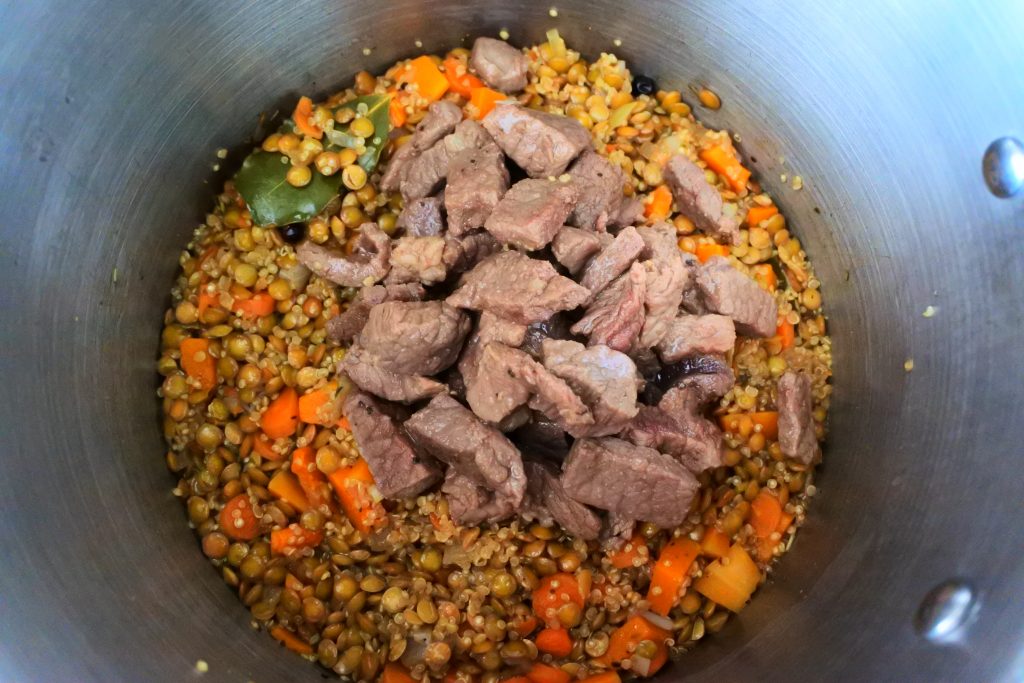 An overhead image of quinoa and lentil and beef stew simmering in a pot with cooked beef added in