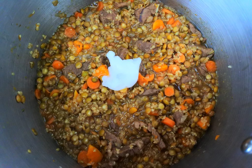 An overhead image of quinoa and lentil and beef stew simmering in a pot with unmelted coconut oil added in
