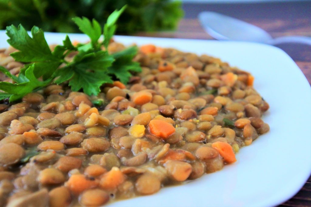 A nearly side view off-center closeup of some parsley nestled atop a bed of coconut lentil stew on a white plate.