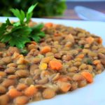 A nearly side view off-center closeup of some parsley nestled atop a bed of coconut lentil stew on a white plate.
