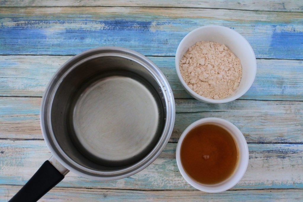 An overhead image of ingredients for a simple honey-sugar syrup including a pot of water, and two dishes, each with sugar and honey