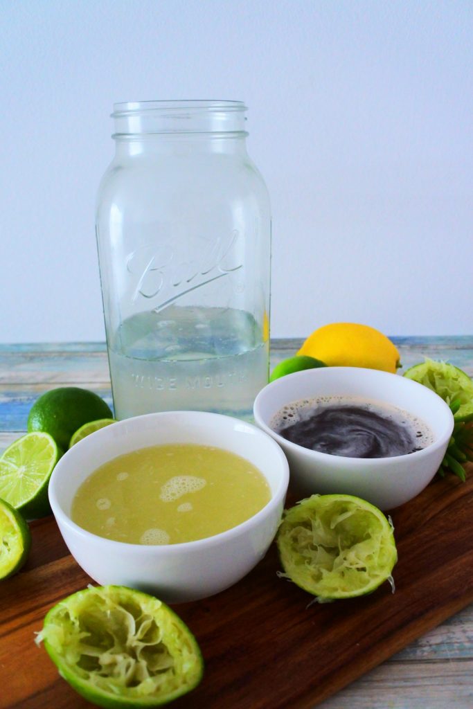 A head on image of ingredients for limeade including water, lime juice and a simple honey and sugar syrup surrounded by fresh limes