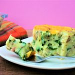A head on image of a piece of next level mashed potatoes casserole on a place with a forkful cut out and next to it