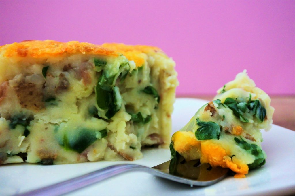 A head on image of a piece of next level mashed potatoes casserole on a place with a forkful cut out and next to it