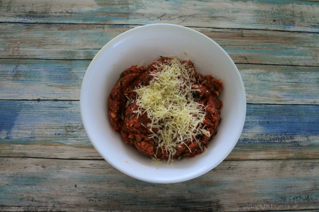 An overhead image of a bowl with meatball mixture with shredded parmesan cheese over it
