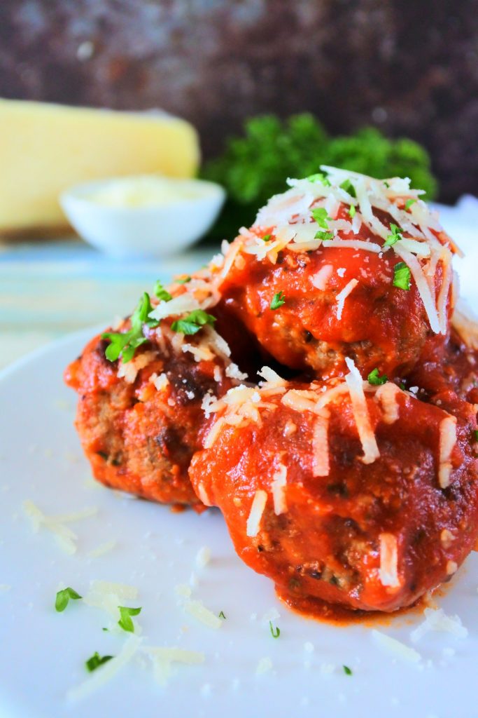 A close up head on image of a small stack of meatballs garnished with shredded cheese and fresh parsley