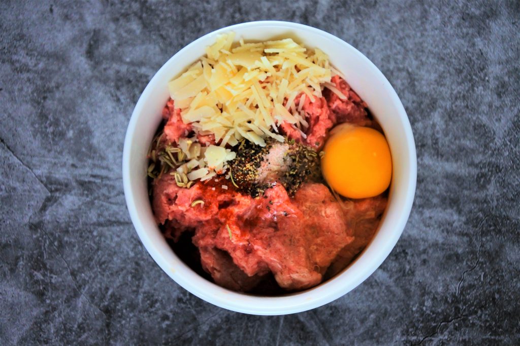 An overhead image of a bowl of ground turkey topped with an egg, Parmesan cheese and dried herbs and spices