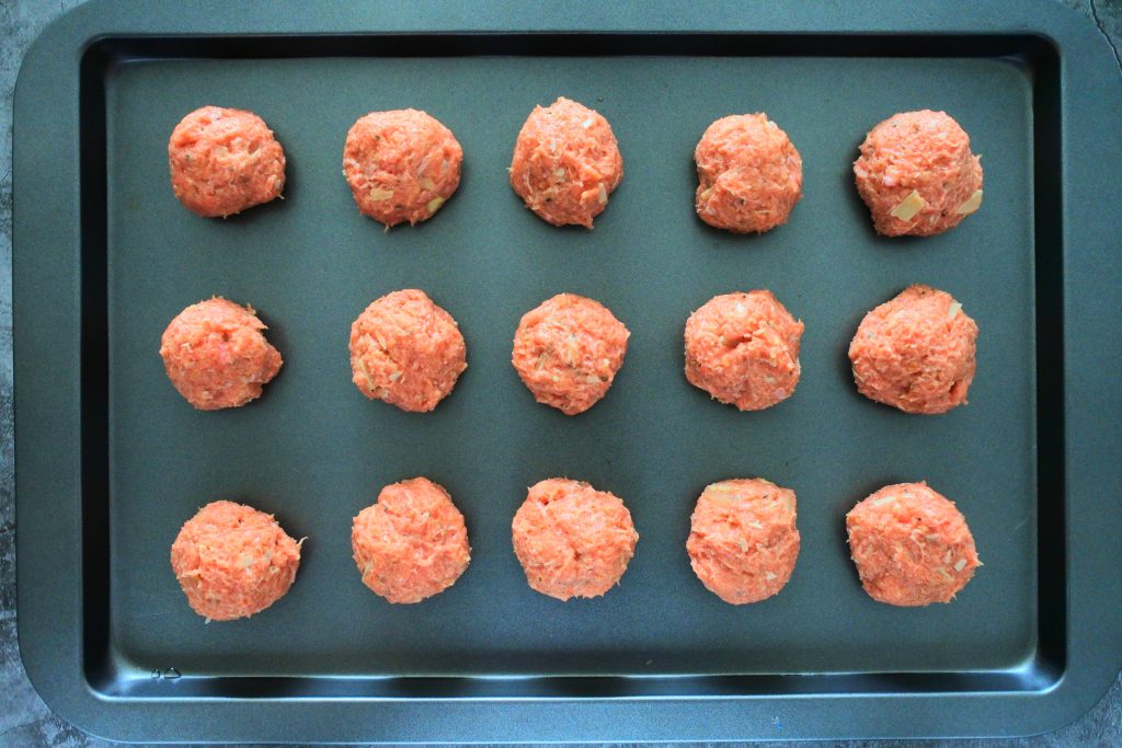 An overhead image of a baking tray with fifteen uncooked turkey meatballs