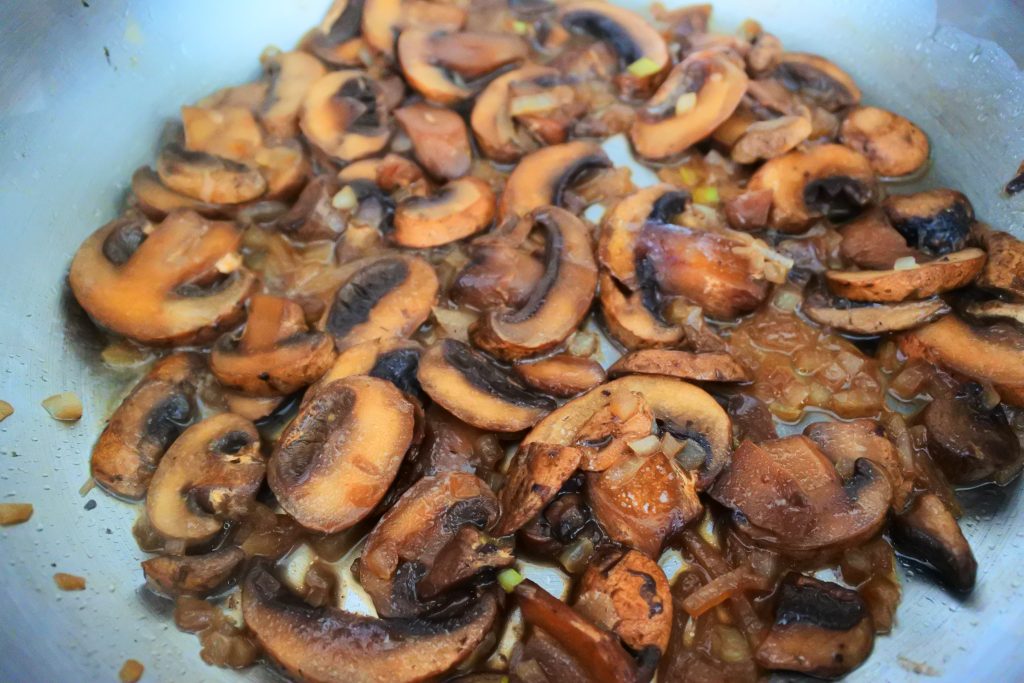 A close up image of onions and mushrooms in a saute-pan