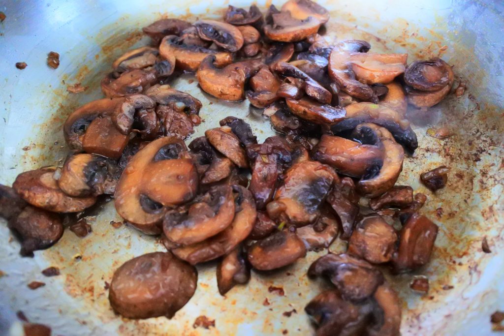 A close up image of caramelized onions and mushrooms in a saute-pan