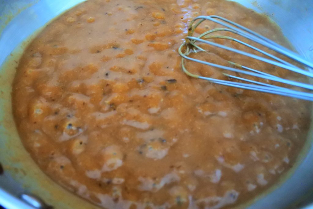 A close up image of a steamy and bubbling saute-pan of gravy with a metal whisk in the top right of the image.
