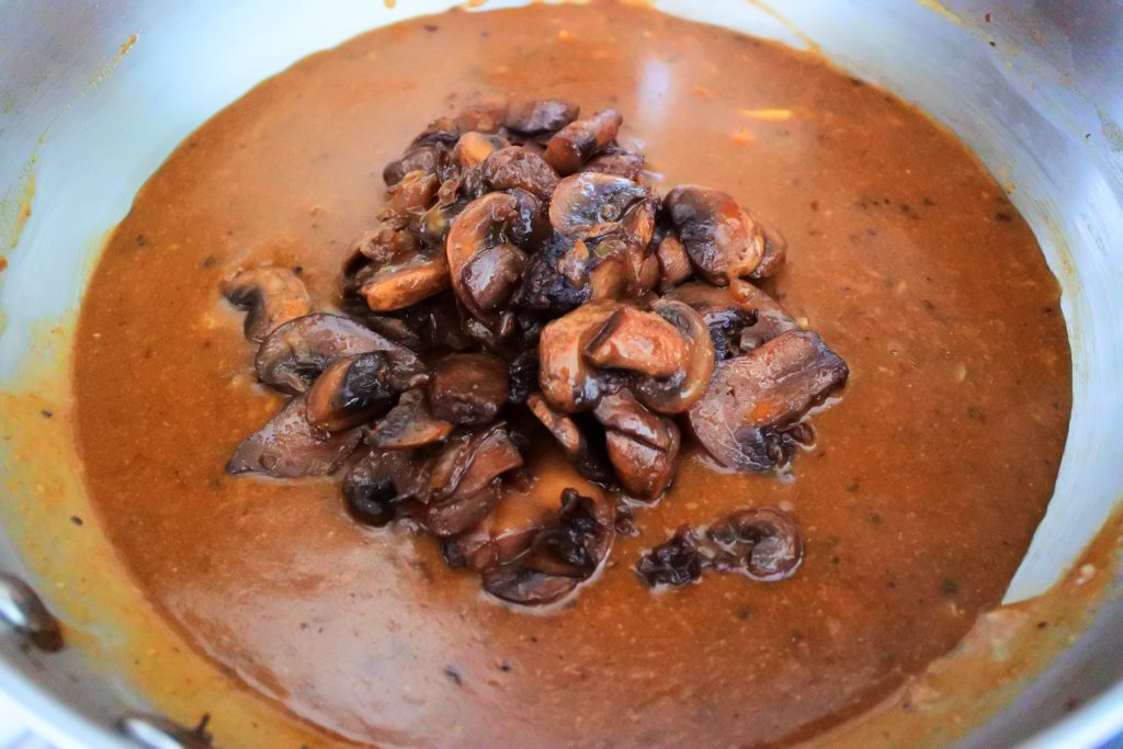 A close up image of a saute-pan of brown gravy with caramelized onions and mushrooms piled in the middle