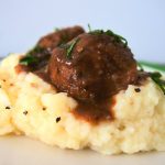 A close up image of a serving of mashed cauliflower topped with two Salisbury meatballs in gravy.
