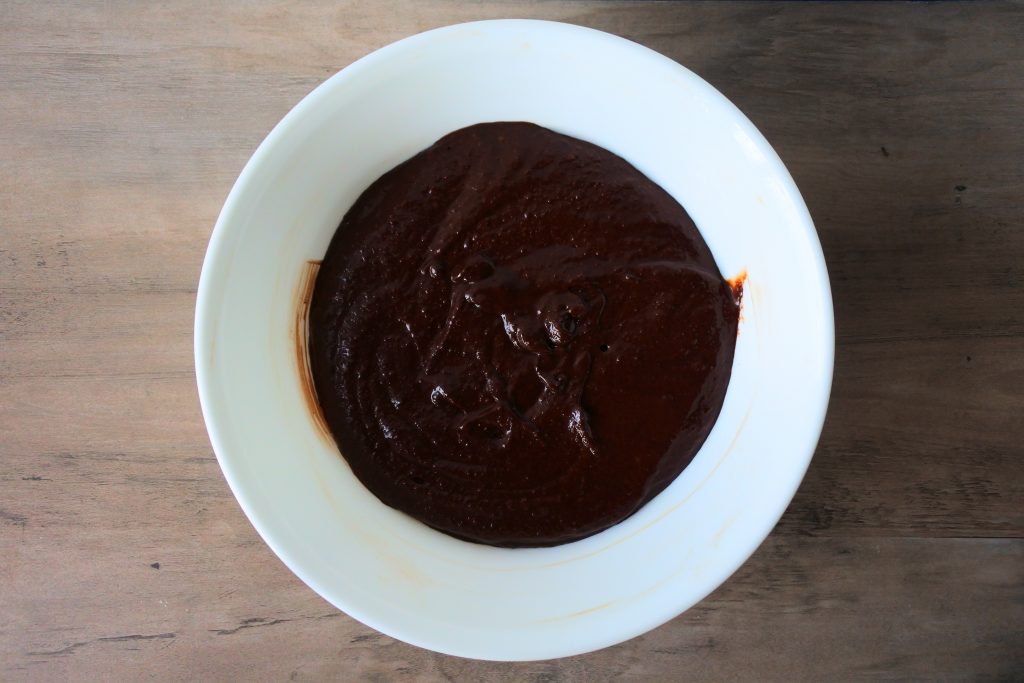 An overhead image of a bowl containing a mixture of melted butter, coconut sugar, vanilla, eggs, cocoa powder, almond flour, baking soda, salt, and a splash of milk.