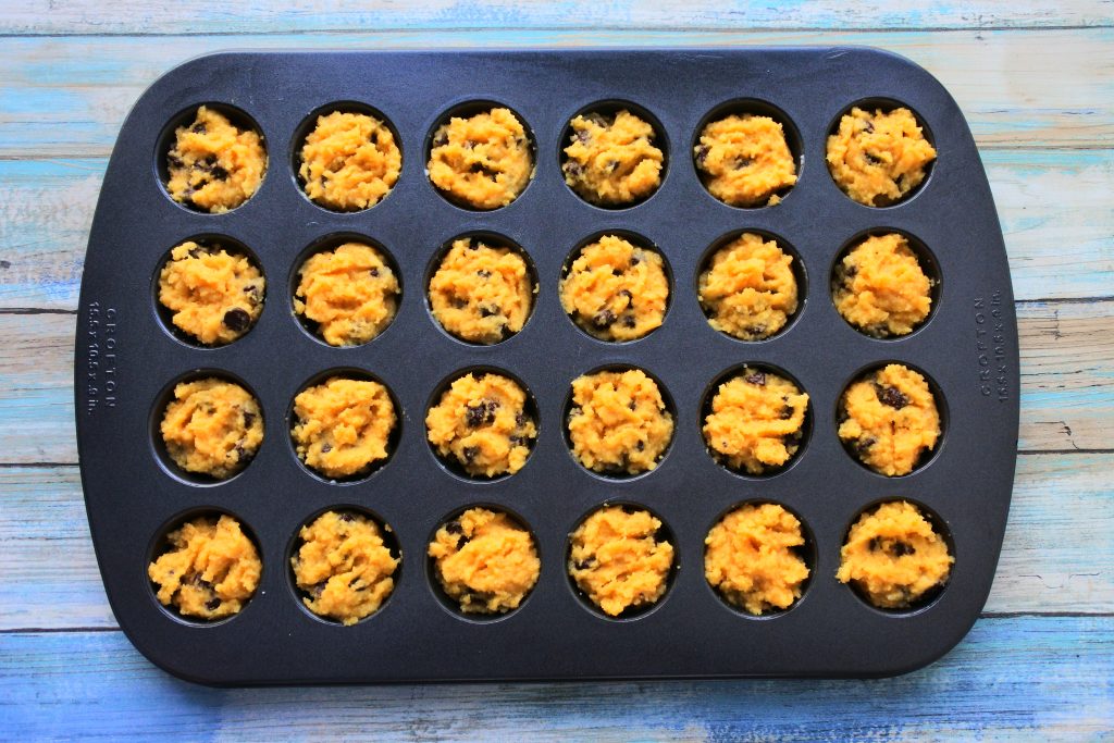 An overhead image of a mini muffin tray filled with chocolate chip muffin batter
