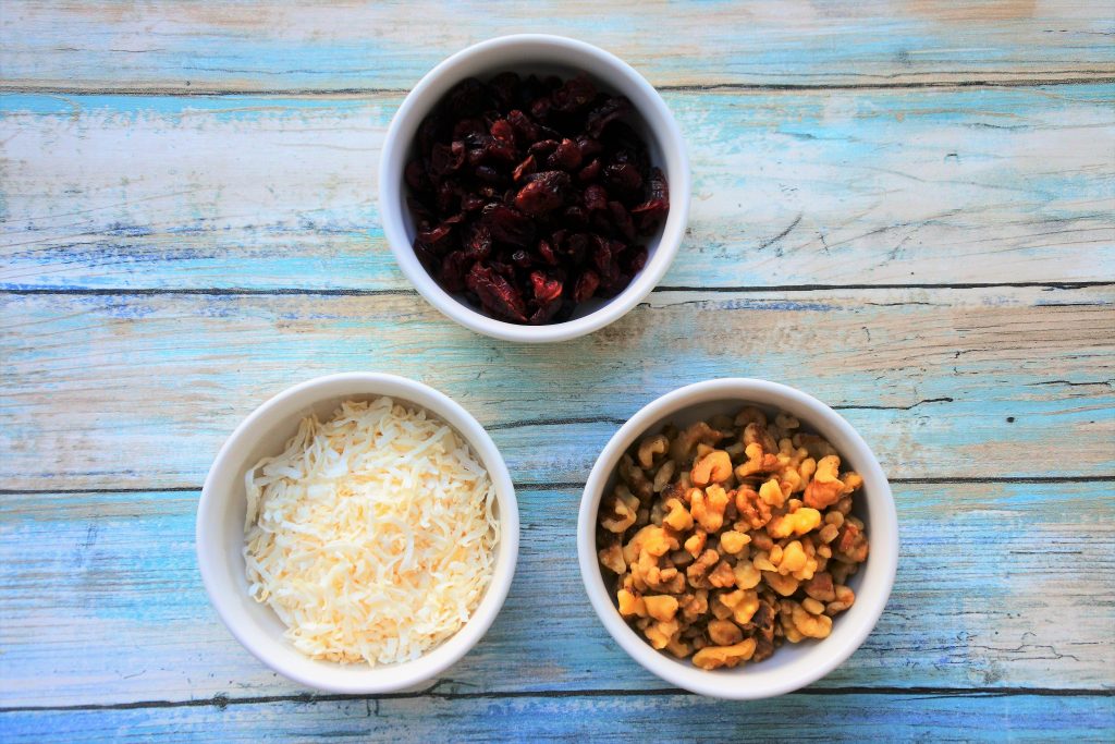 An overhead image of three bowls containing dried cranberries, shredded coconut and walnut pieces
