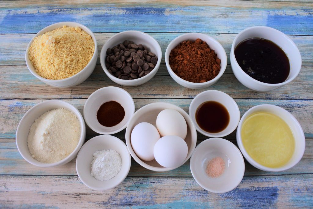 An overhead image of bowls of ingredients for Gluten Free Double Chocolate Chip Muffins including almond flour, coconut flour, chocolate chips, cocoa powder, maple syrup, extra light olive oil, vanilla extract, salt, eggs, espresso powder and baking powder