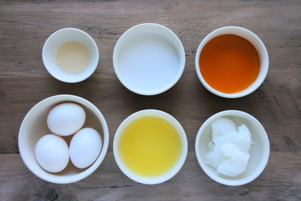 An overhead image of bowls containing eggs, lemon juice, coconut oil, honey, coconut milk, and vanilla extract.
