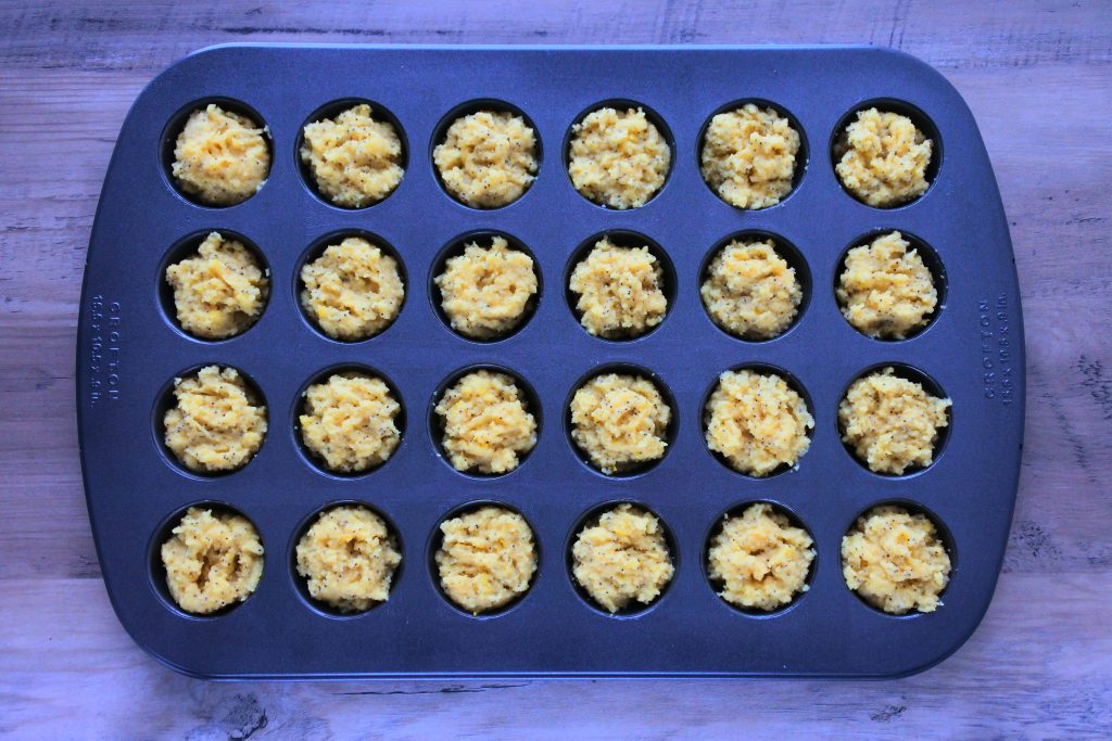 An overhead image of a mini muffin tray filled with lemon poppyseed muffin batter