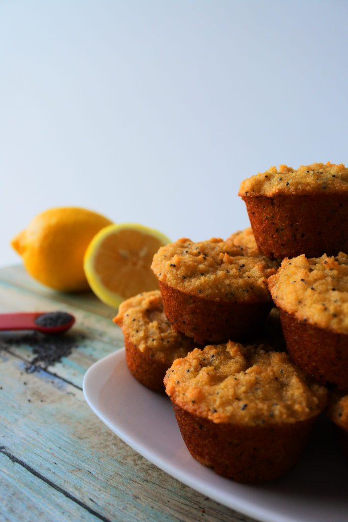 A head on image of a stack of mini lemon poppyseed muffins on a plate with a lemon and teaspoon measure of poppyseeds in the background
