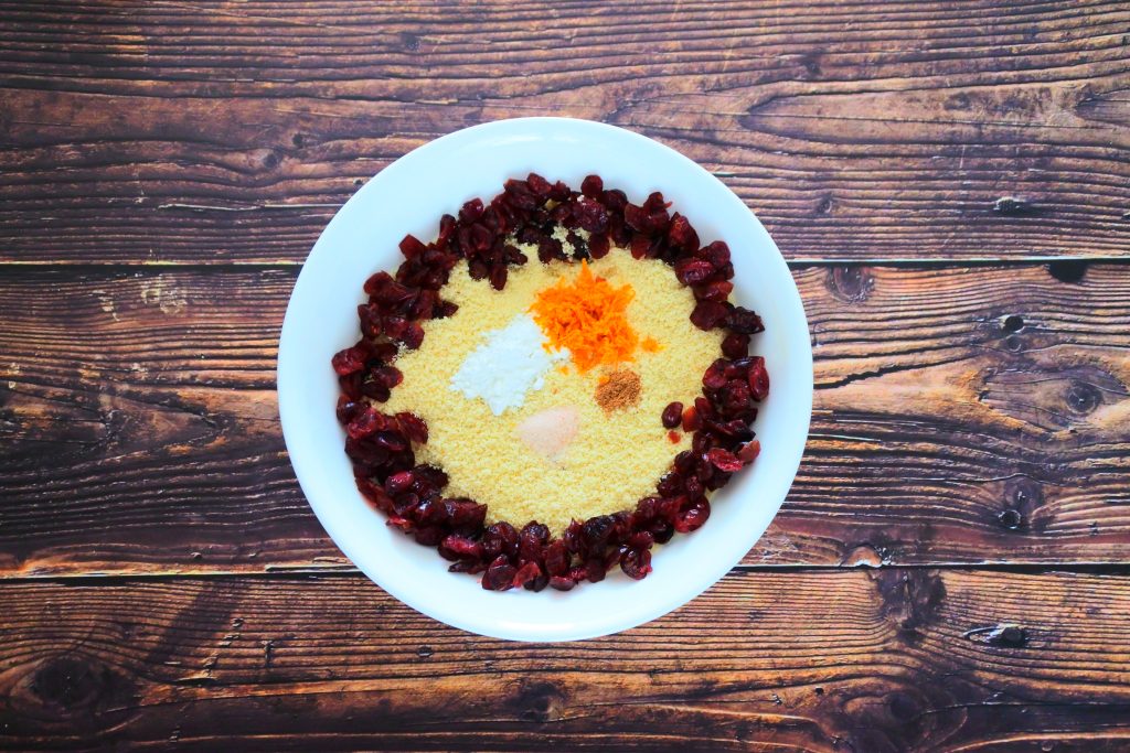 An overhead image of a bowl of almond flour surrounded by dried cranberries as well as salt, nutmeg, orange zest and baking powder.