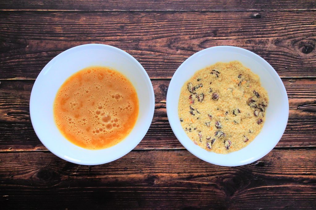 An overhead image of two bowls of mixed wet and mixed dry ingredients for an orange cranberry muffin batter