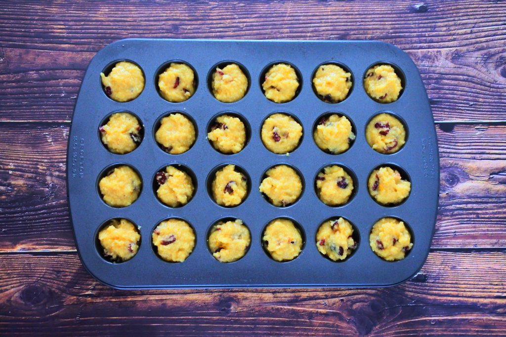 An overhead image of a mini muffin tray filled with orange cranberry muffin batter