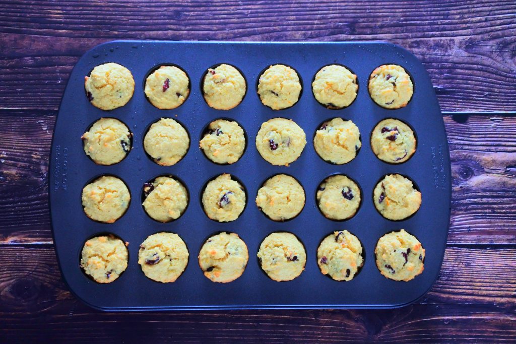 An overhead image of a mini muffin tray filled with baked orange cranberry muffin