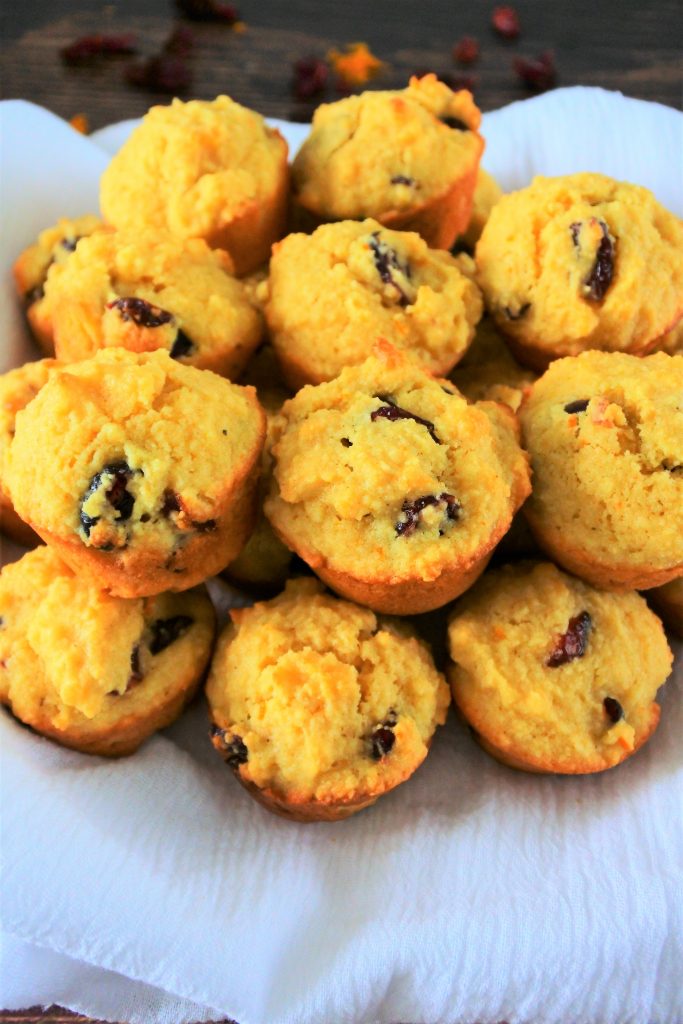 A close up image of a pile of orange cranberry mini muffins on a white cloth.