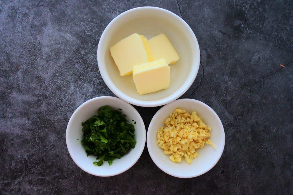 An overhead image of three bowls containing pats of butter, minced garlic and cilantro