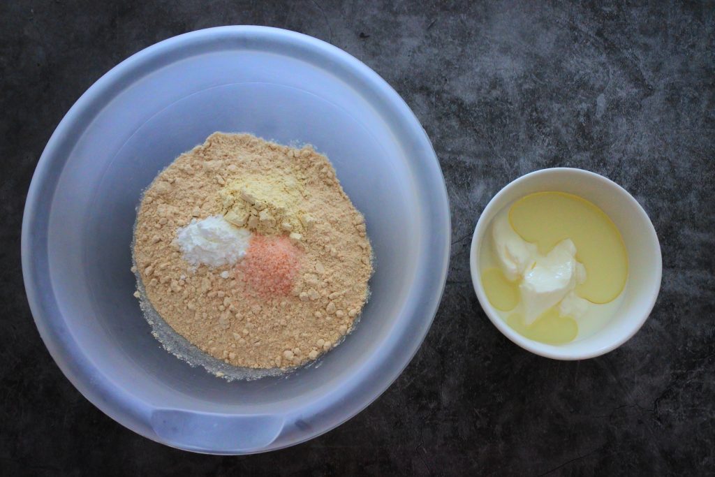 An overhead image of a bowl of whole wheat flour, salt, baking powder and vital wheat gluten and another bowl of milk, oil and yogurt.