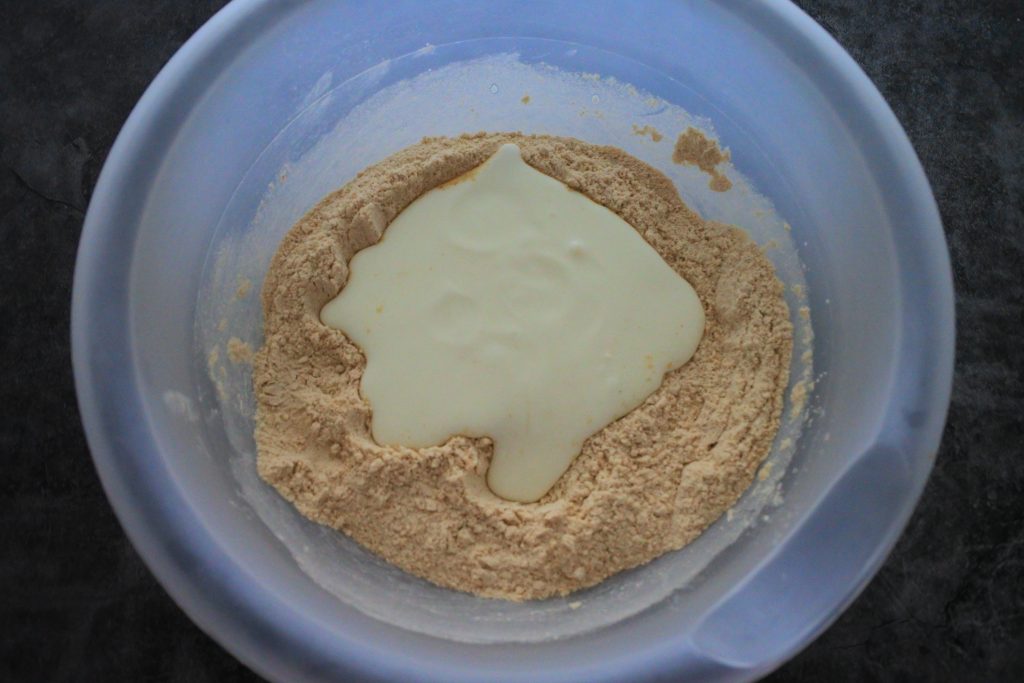 An overhead image of a bowl with flour and a poured yogurt mixture on it.