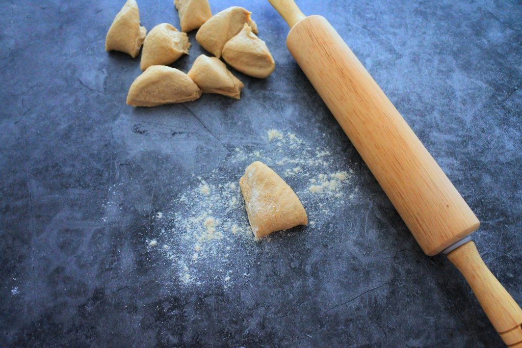 An overhead image of pieces of unrolled naan dough and a rolling pin on a floured surface